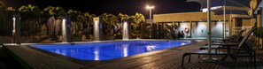 A nighttime swimming pool with a wooden deck and lounge chairs. - Crown Hotel (Port Moresby)