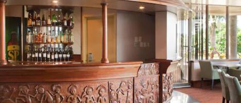 A bar area with a curved wooden counter and a view of the outdoors through large windows.