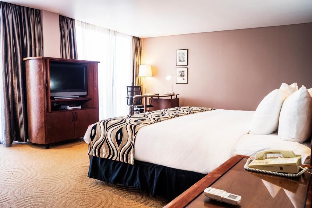 A hotel room with a large bed, a TV, a desk with a lamp, and a telephone on a side table.