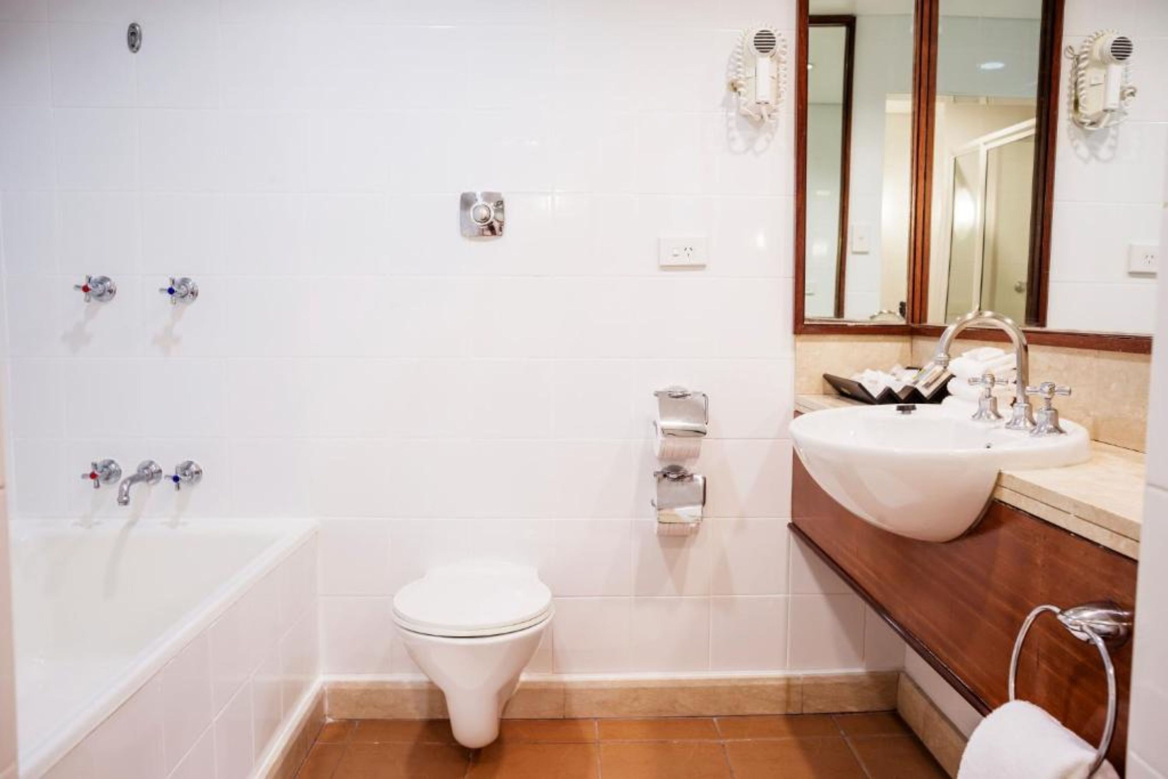 A modern bathroom with a white bathtub, a white toilet, a sink with a mirror, and a towel rack.