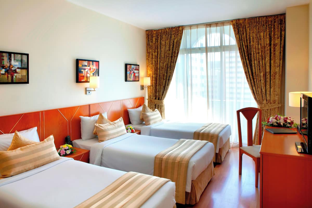 Una habitación de hotel con dos camas, un escritorio, una silla y un ventanal con cortinas.