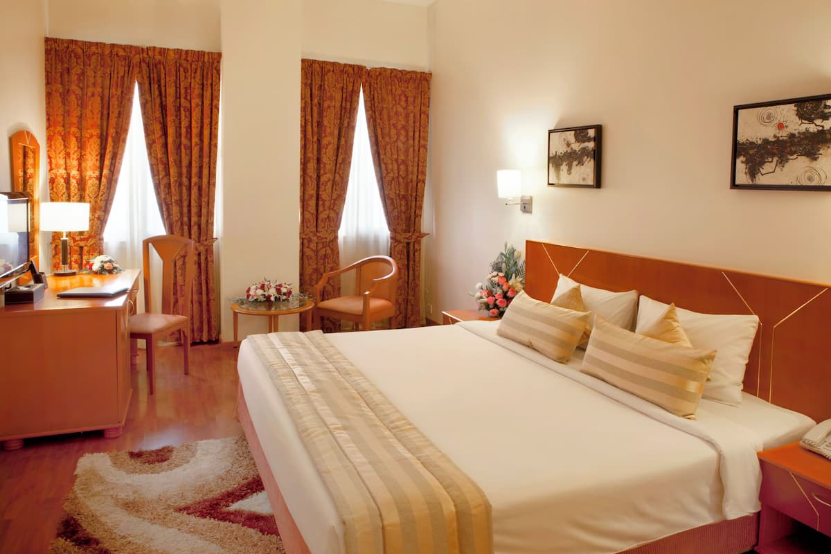 Una habitación de hotel con una cama, un escritorio, una silla, una mesita de noche y una pequeña mesa con una lámpara y flores.