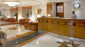 A hotel reception area with a reception desk, a large clock, and a seating area with chairs and tables. - Landmark Hotel (Dubai)