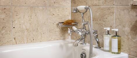 A bathroom with a bathtub, a handheld showerhead, and two bottles of liquid soap on the edge of the tub.