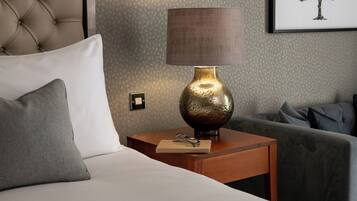 A neatly made bed with a white pillow, a small wooden nightstand with a brass lamp, and a framed picture on the wall.