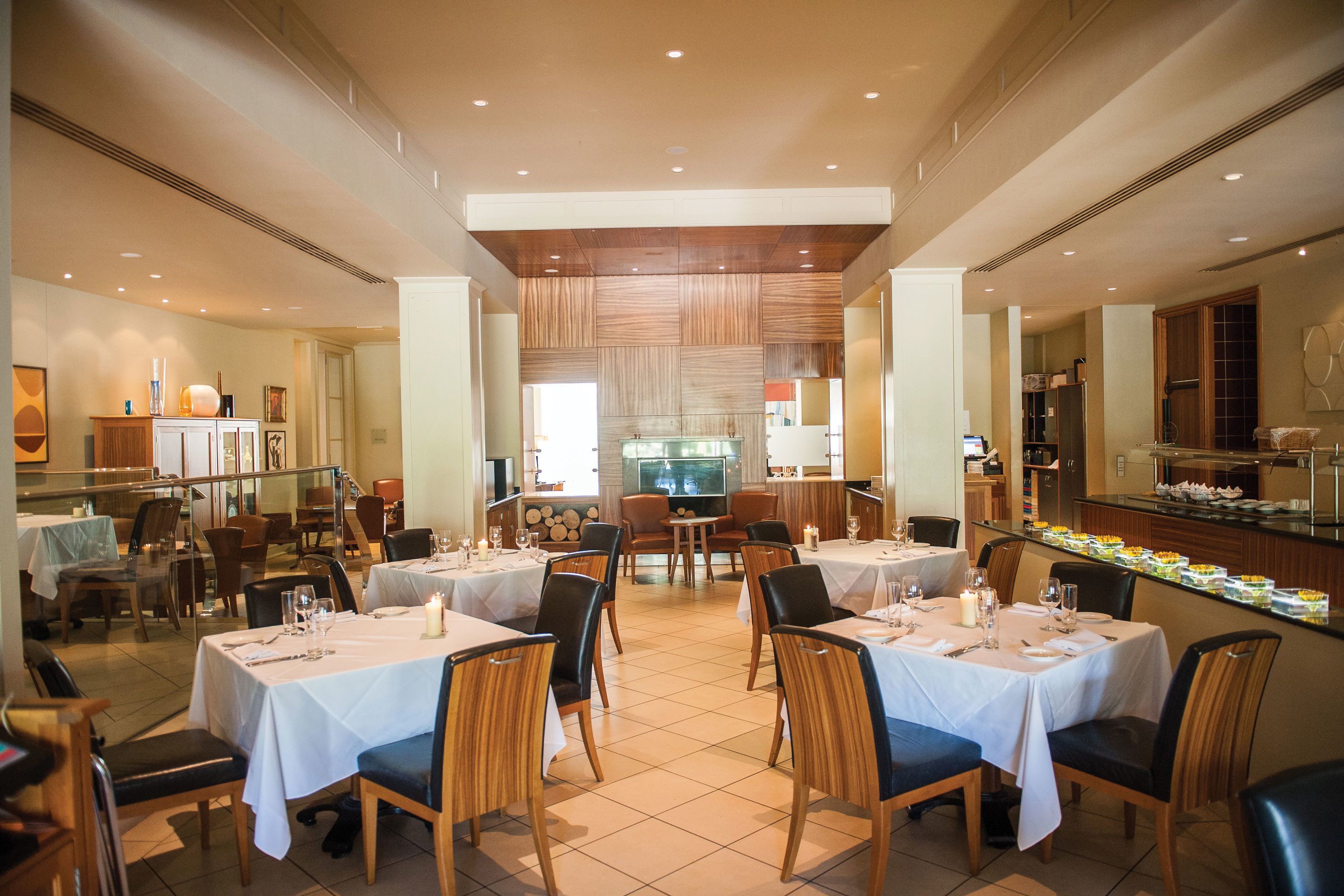 Un ristorante spazioso con numerosi tavoli e sedie, una zona pranzo centrale e una cucina visibile sullo sfondo.