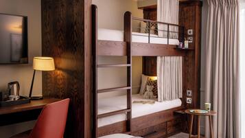 A bunk bed room with a desk, chair, lamp, and a small table with a plate.