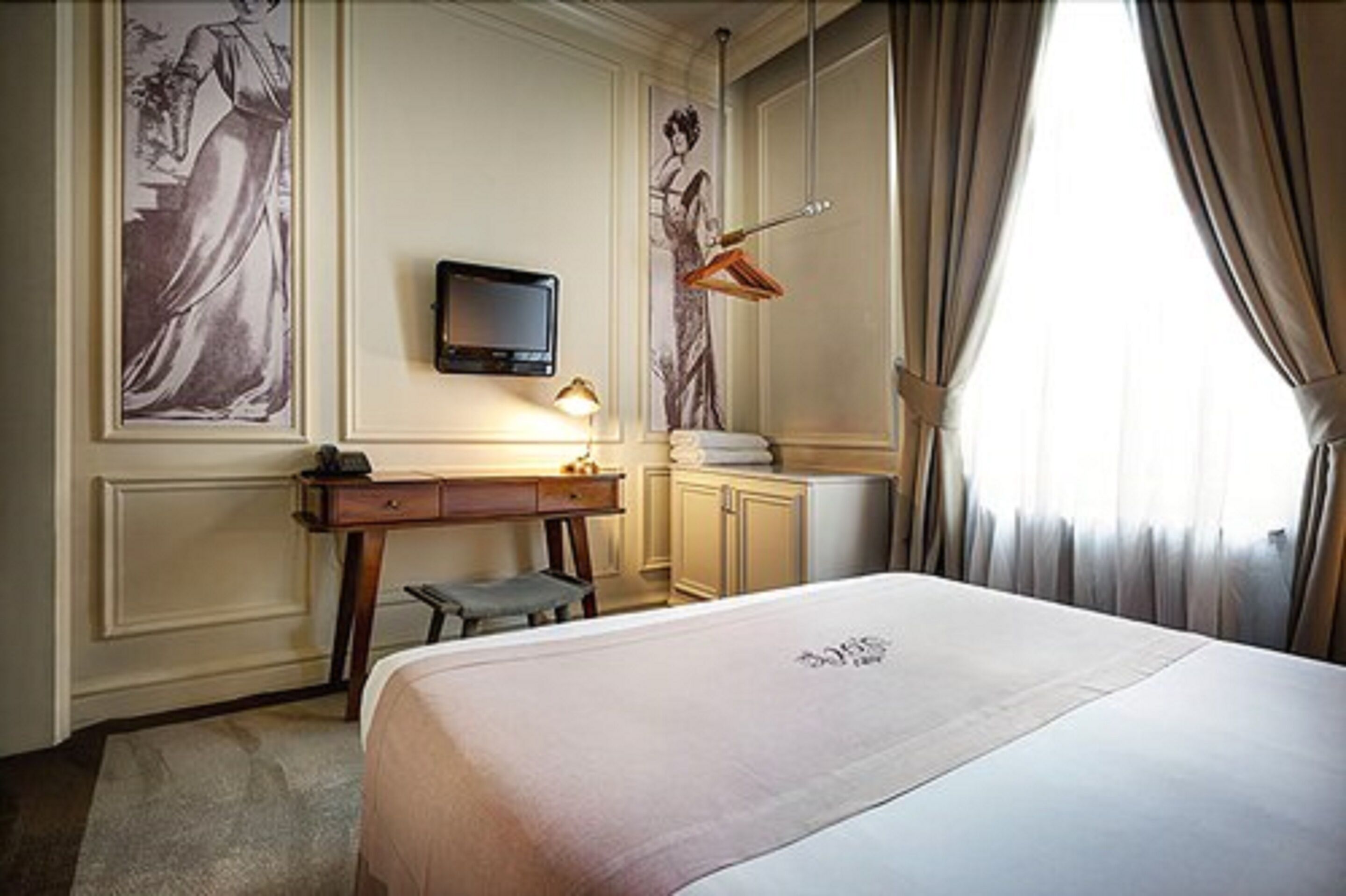 A hotel room with a bed, a desk, a chair, a television, and a window with curtains.