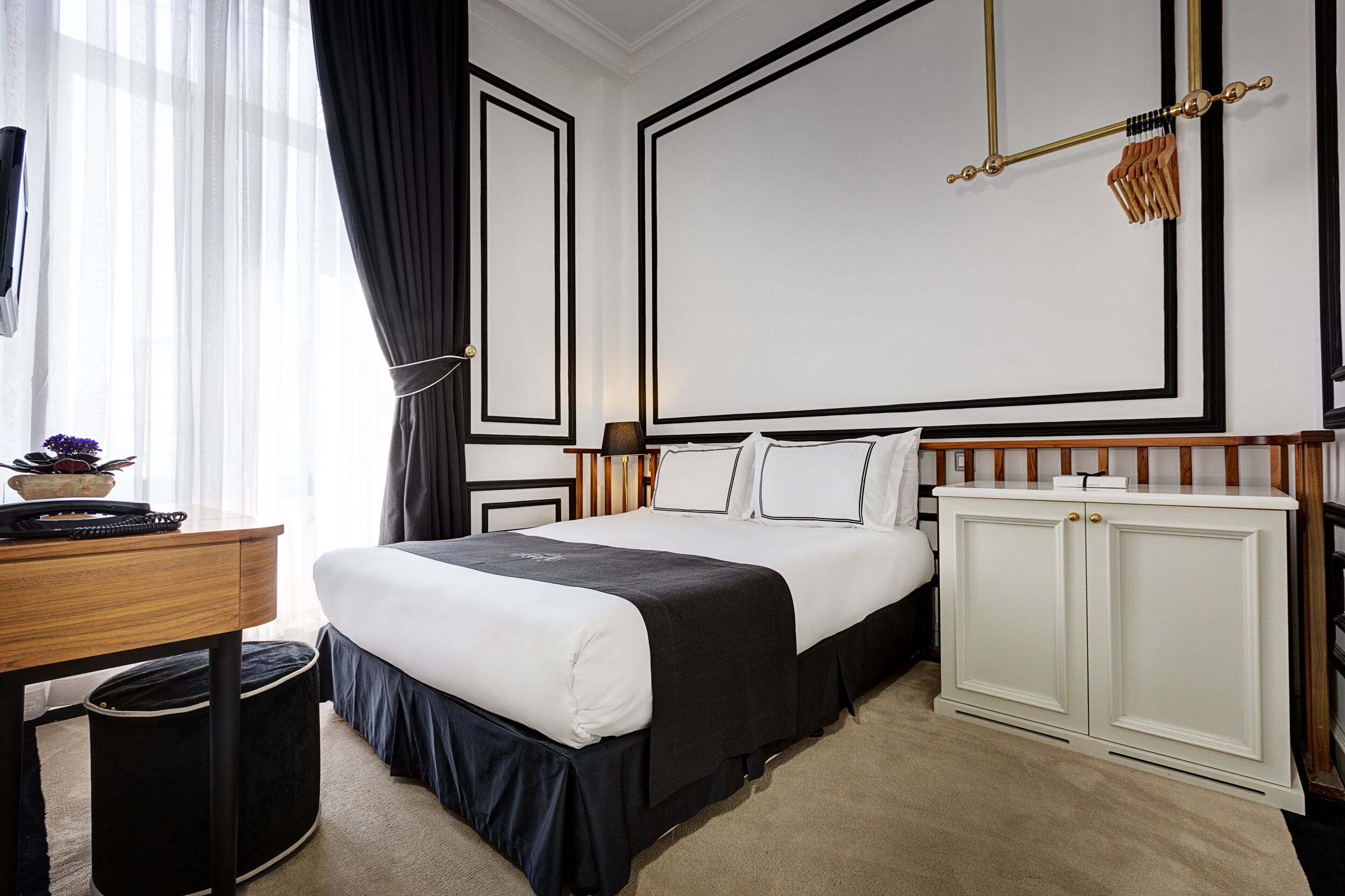 Een keurig opgemaakt hotelkamer met een bed, nachtkastje en een garderobe.