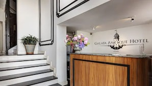 Un espace d’accueil avec un bureau en bois, un lustre et une enseigne indiquant «Galata Antique Hotel».