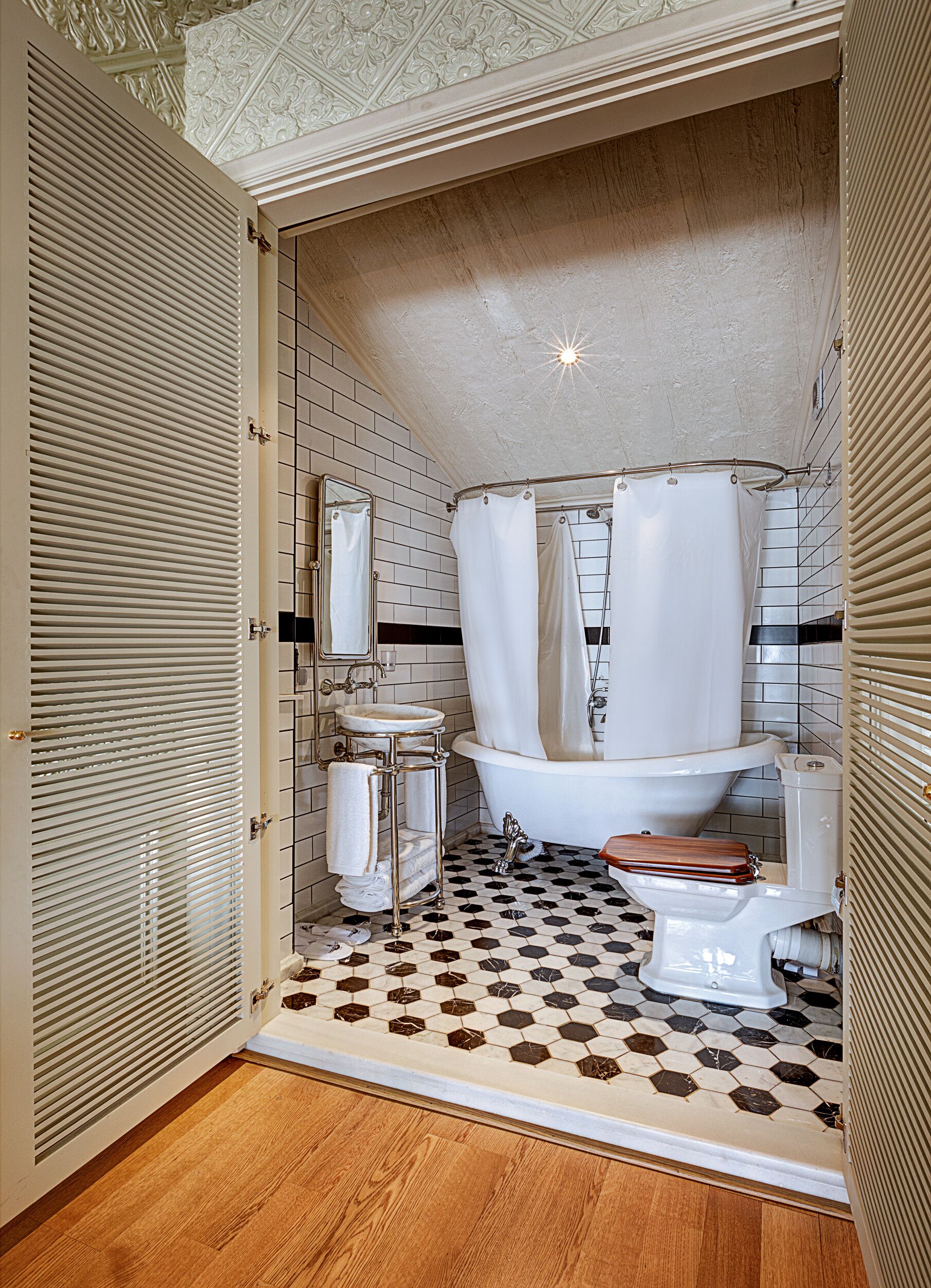 A bathroom with a white toilet, a sink with a mirror, a shower with a curtain, and a tiled floor with a hexagonal pattern.