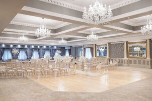 Un amplio salón con filas de sillas, candelabros y grandes ventanales.