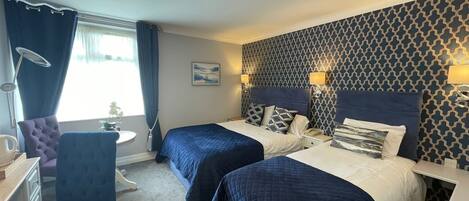 A hotel room with two beds, a desk, a chair, and a patterned wall.