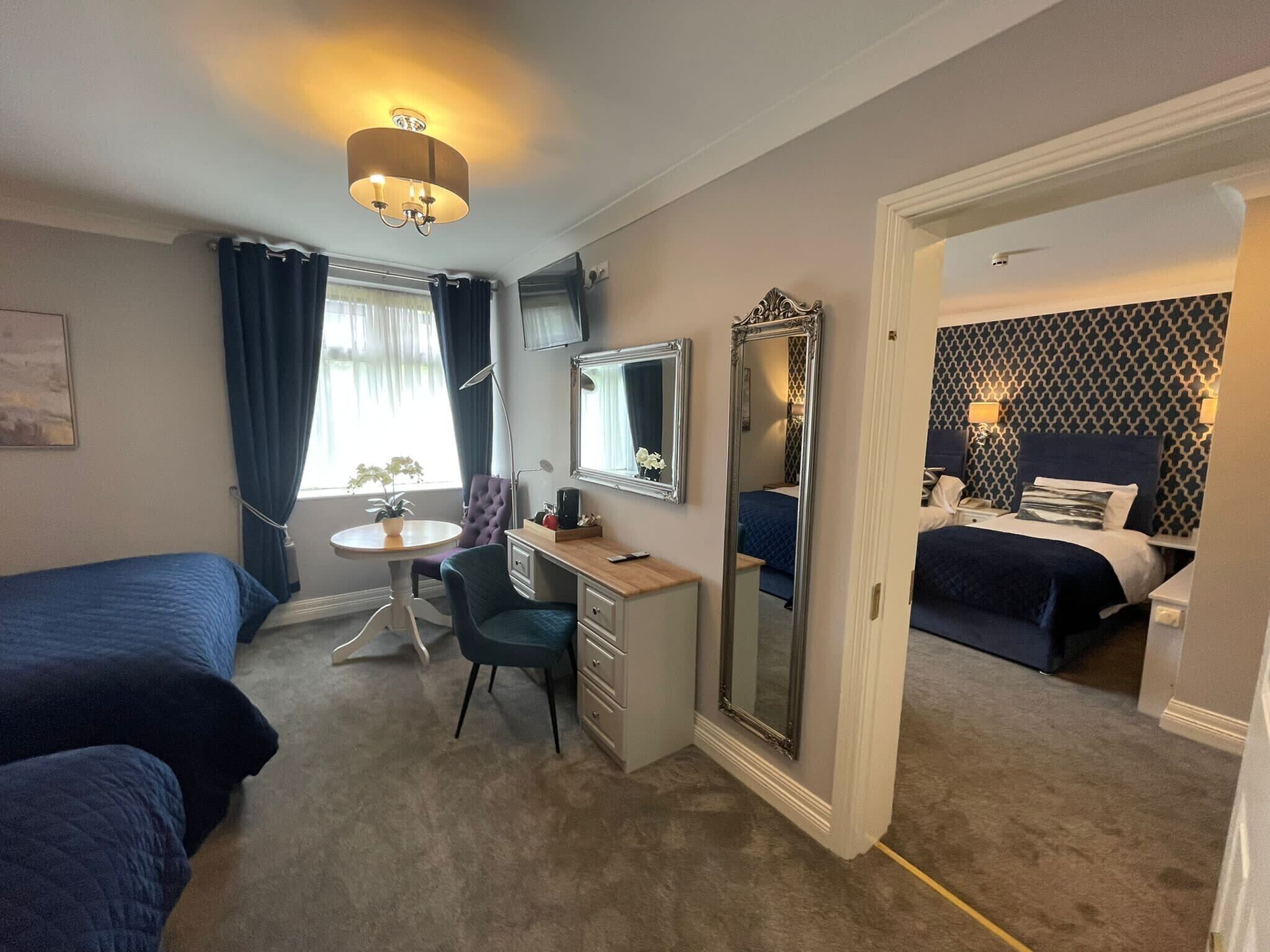 A hotel room with two beds, a desk, a chair, a mirror, and a window with curtains.