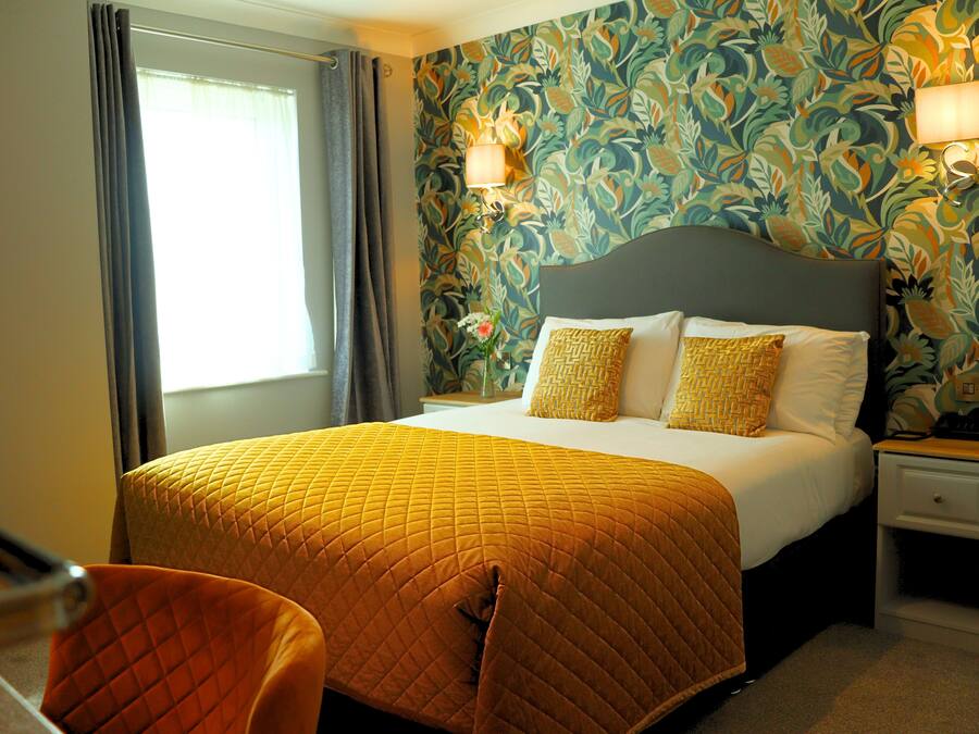 A hotel room with a bed, a nightstand, a chair, and a window with curtains.