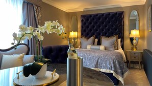 A luxurious hotel room with a large bed, a sitting area, and a dining table with a vase of orchids. - Ardboyne Hotel (Navan)
