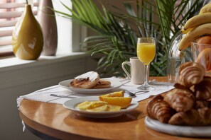 A breakfast table with croissants, orange slices, a glass of orange juice, and a plate of eggs.
