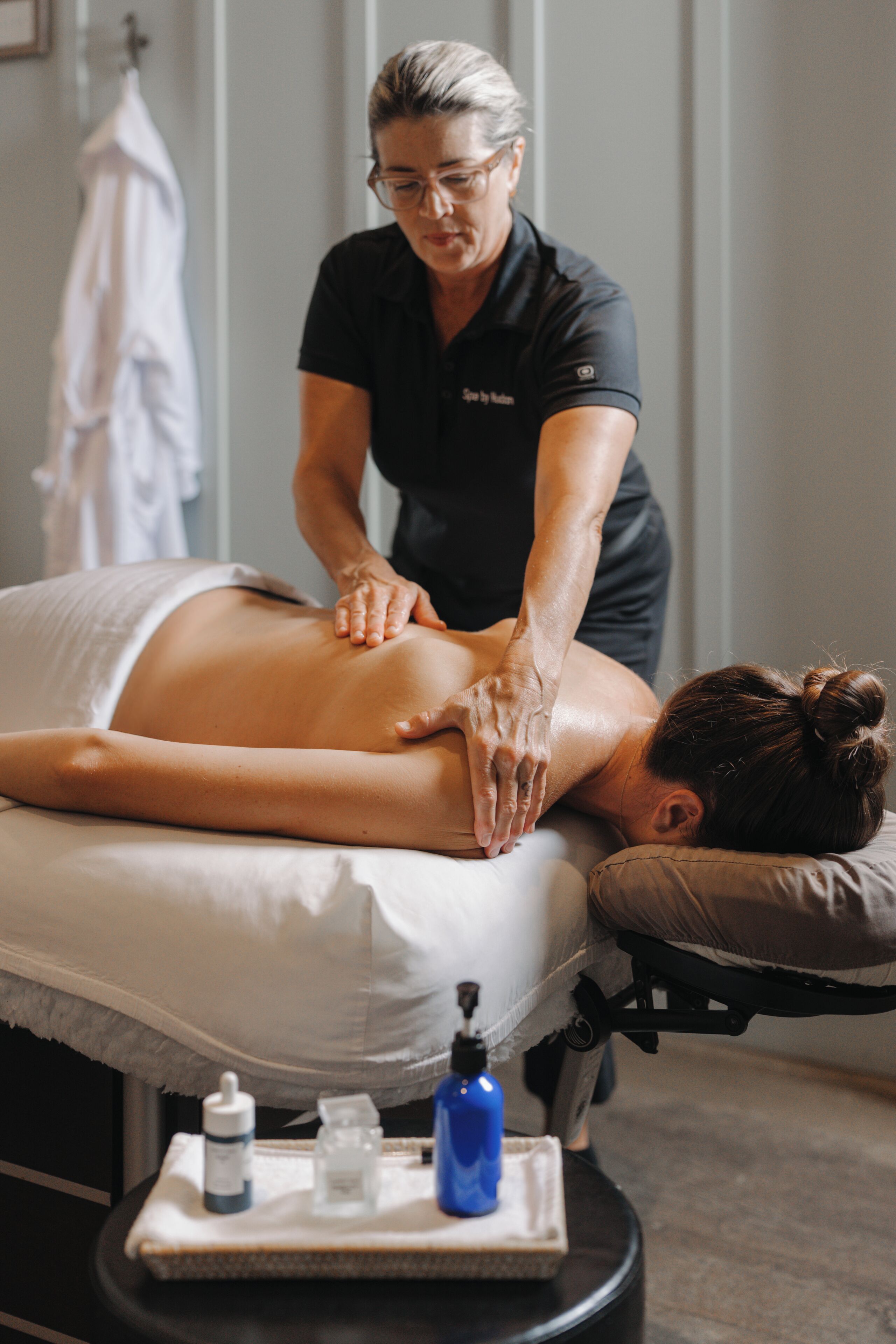 A massage therapy session in a room with a massage table, a towel, and a tray with bottles.