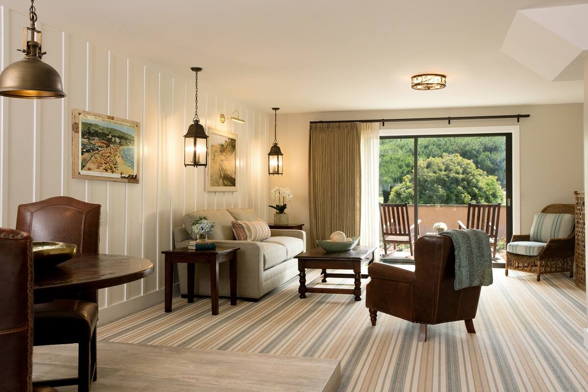 A spacious living room with a large window, a dining area with a table and chairs, and a cozy seating area with a sofa and armchairs.