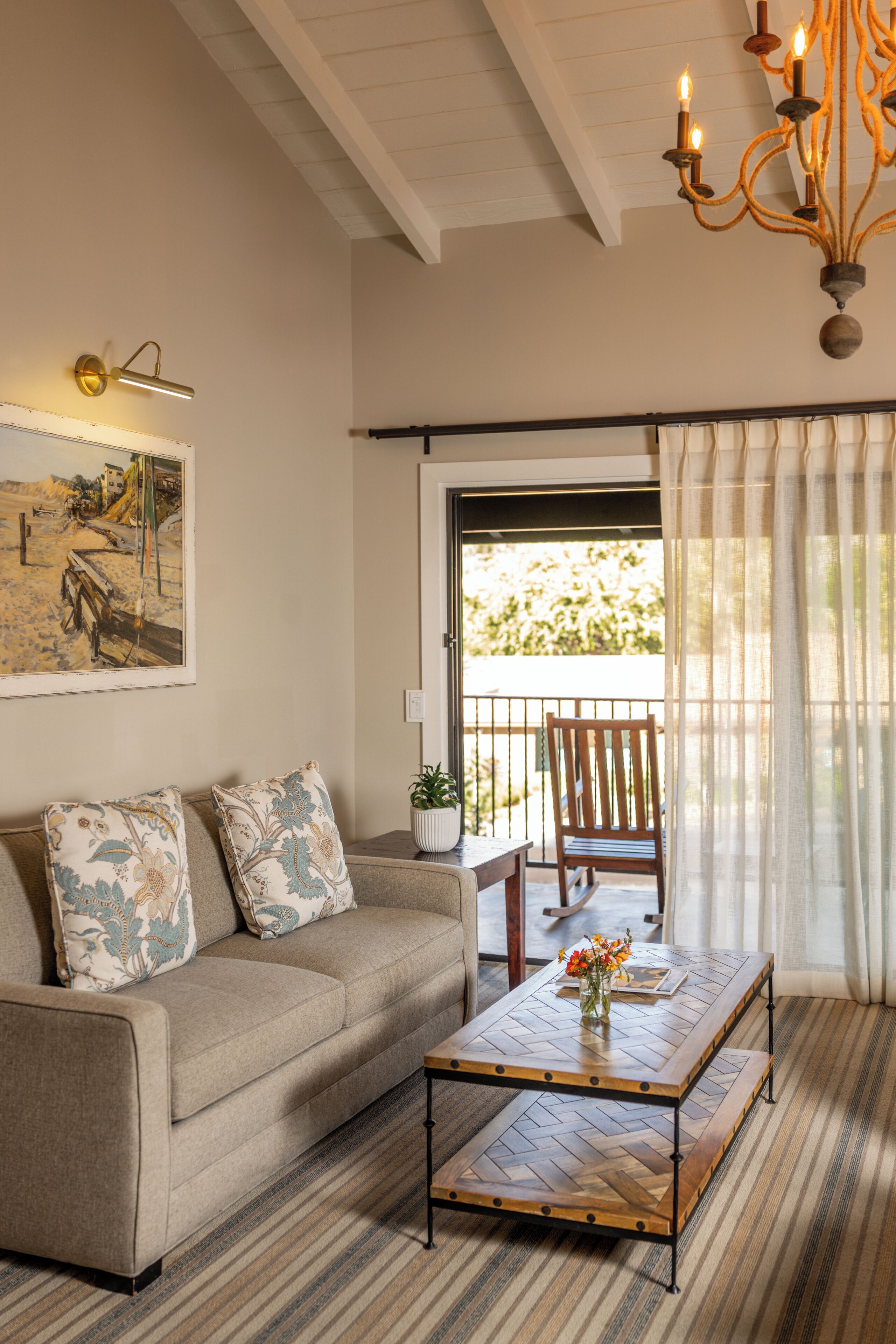 A living room with a sofa, a coffee table, a painting, and a view through a window.