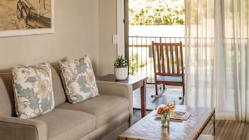 A living room with a sofa, a coffee table, a painting, and a view through a window.