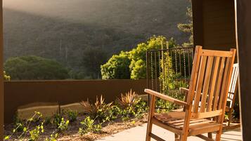A wooden rocking chair on a balcony overlooking a mountainous landscape with a garden in the foreground.