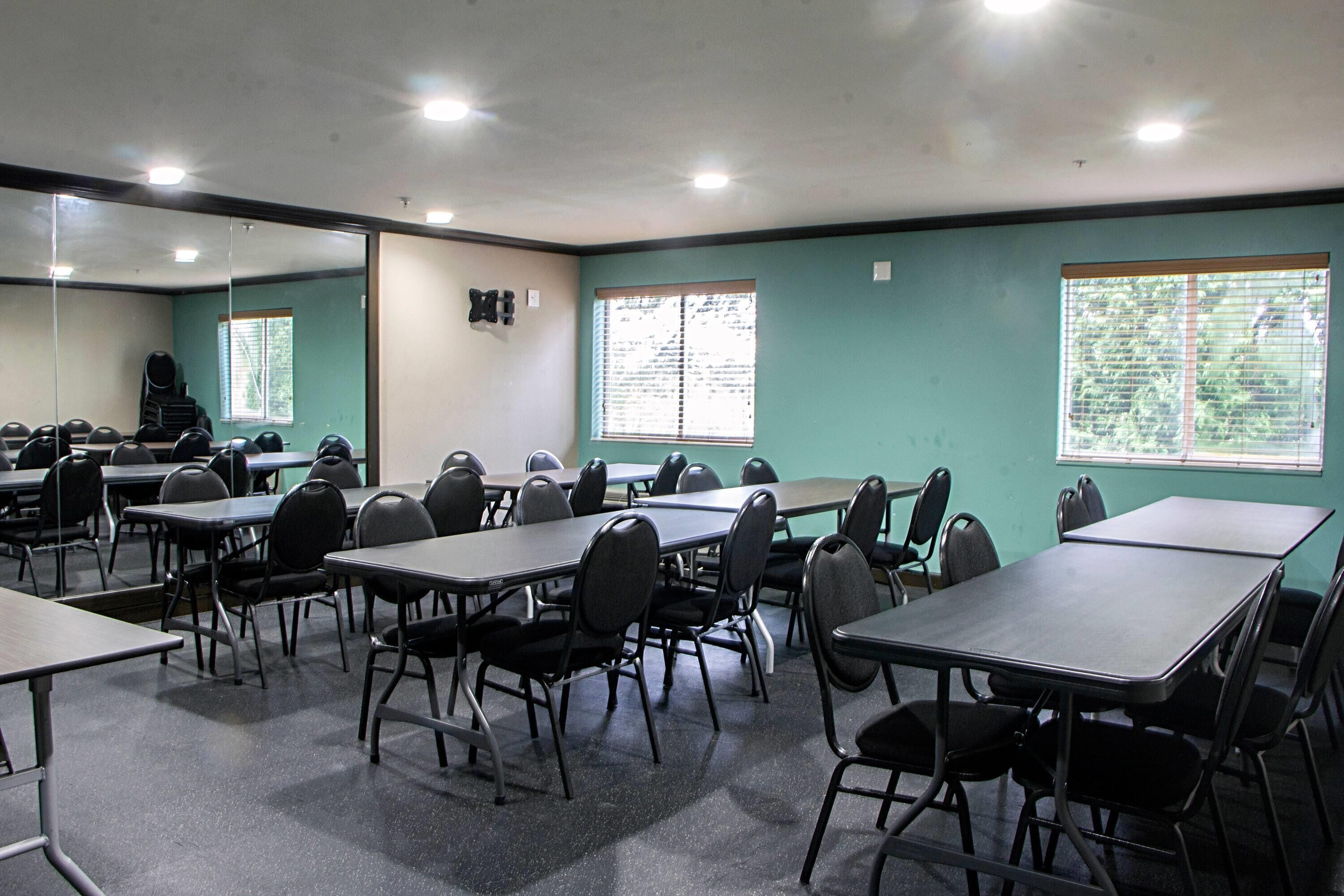 A conference room with tables and chairs, large windows with blinds, and a mirror on the wall.