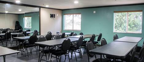 Un salón de conferencias con mesas y sillas, amplias ventanas con persianas y un espejo en la pared.