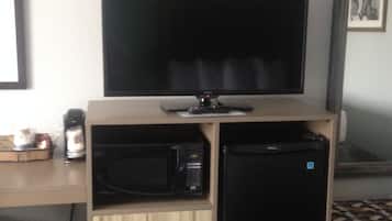 A compact kitchenette with a microwave, refrigerator, and a flat-screen TV on a wooden cabinet.