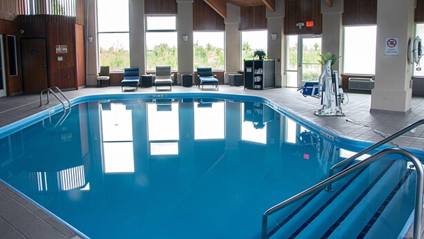 Piscina interior com aviso de proibição de mergulhos, iluminada por grandes janelas e equipada com espreguiçadeiras e um toboágua.