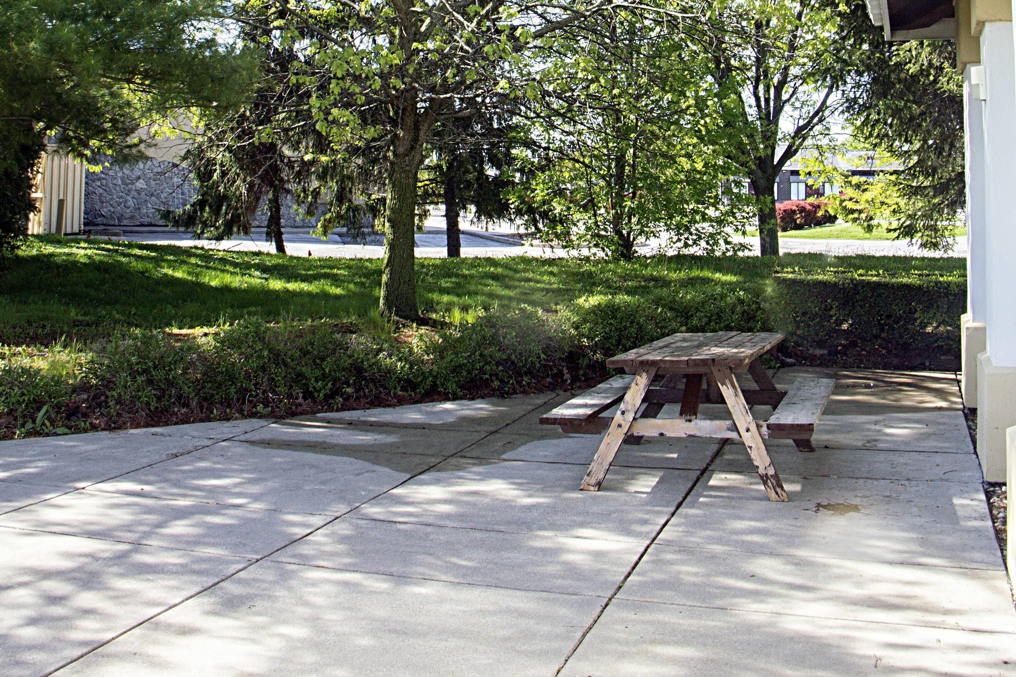 Une table de pique-nique sur une terrasse en béton, avec un mur de pierres et des arbres en arrière-plan.