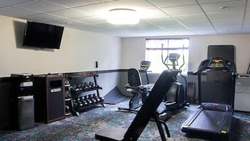 Un gimnasio con cinta de correr, elíptica, bicicleta estática y pesas libres.