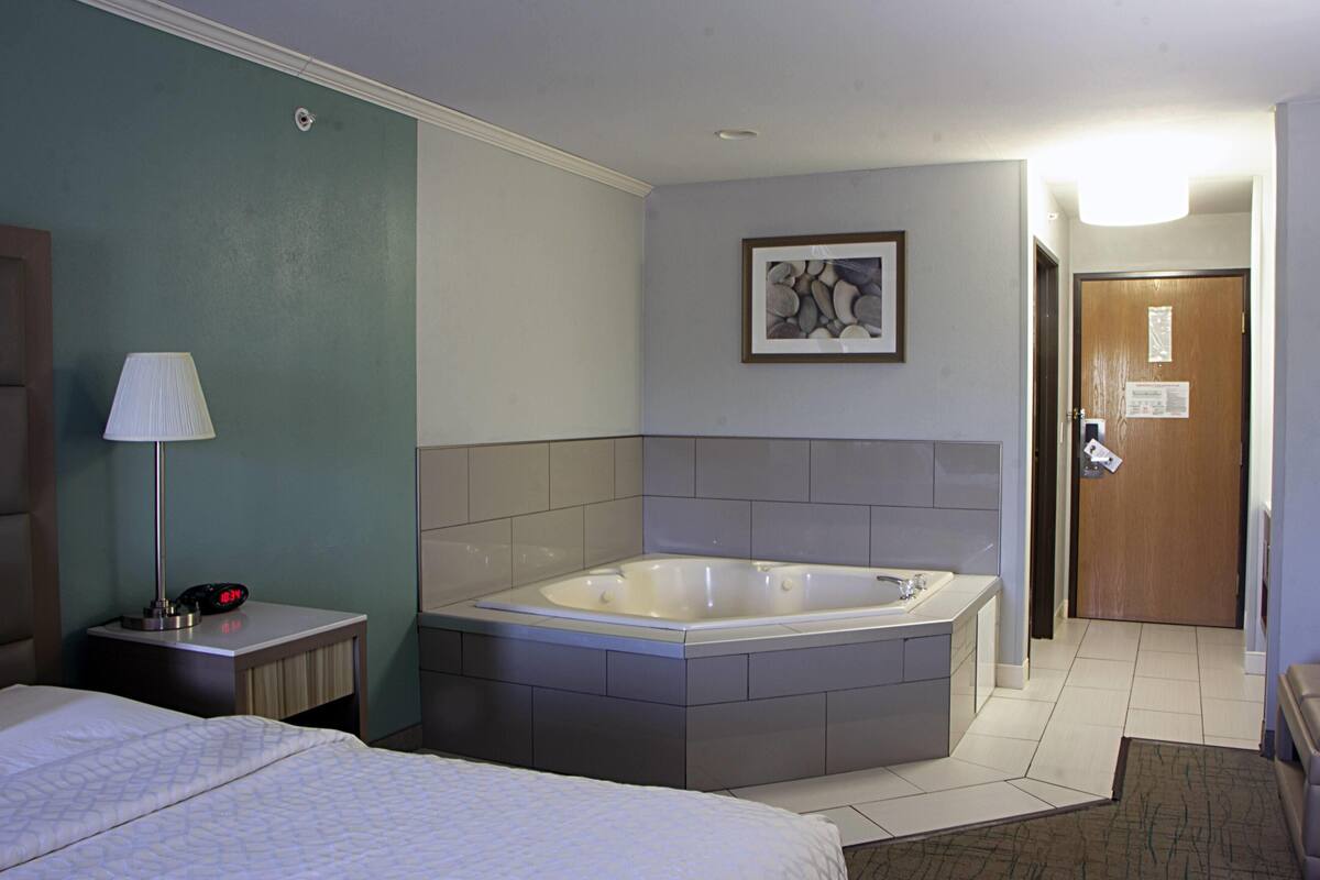 Une chambre d’hôtel avec une grande baignoire, un lit, une table de chevet avec une lampe et un tableau encadré au mur.