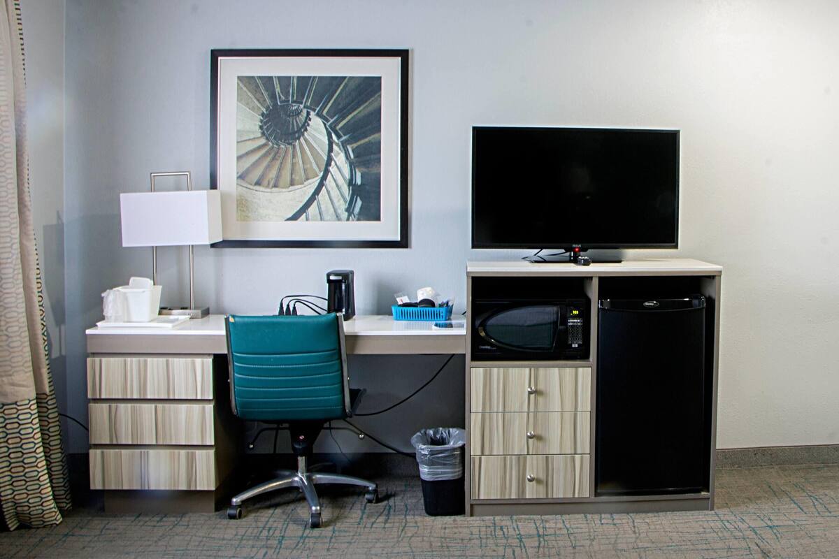 Une chambre d’hôtel équipée d’un bureau, d’une chaise, d’une télévision, d’un four à micro-ondes et d’une poubelle.