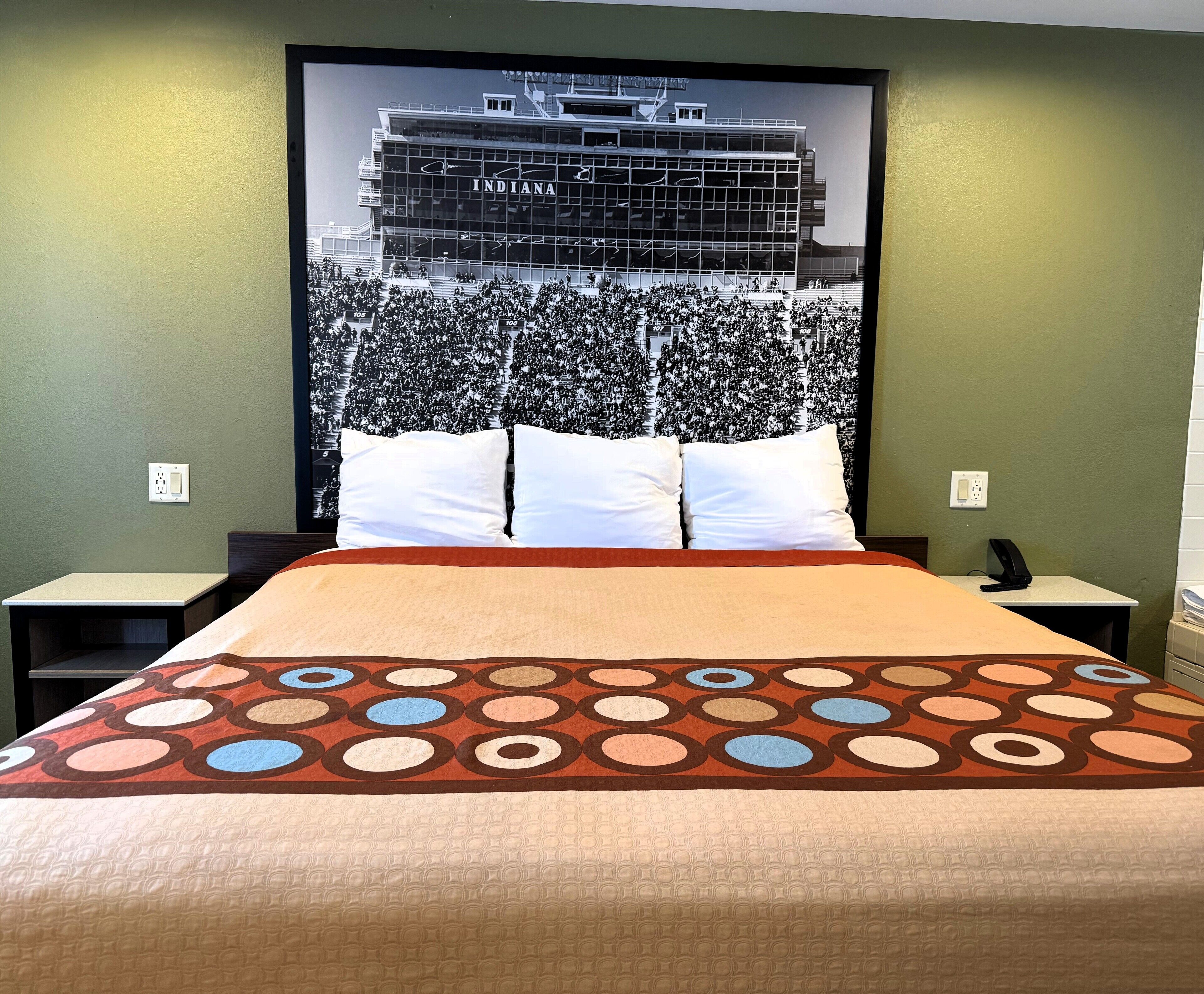 A hotel room with a bed, two bedside tables, a large framed picture of a building, and green walls.