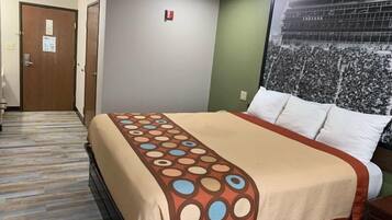 A hotel room with a bed, a wooden floor, a door, and a poster on the wall.