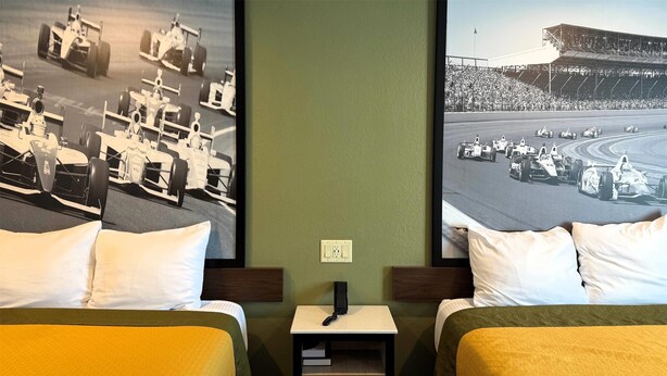 Habitación de hotel con dos camas, una mesita de noche con un teléfono y dos grandes carteles de coches de carreras en la pared.