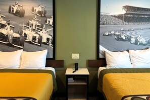 Habitación de hotel con dos camas, una mesita de noche con un teléfono y dos grandes carteles de coches de carreras en la pared.