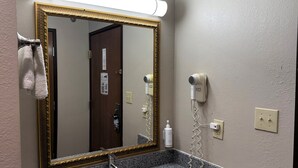 Un baño con lavamanos de encimera de granito, espejo con marco dorado, secador de pelo y toallero.