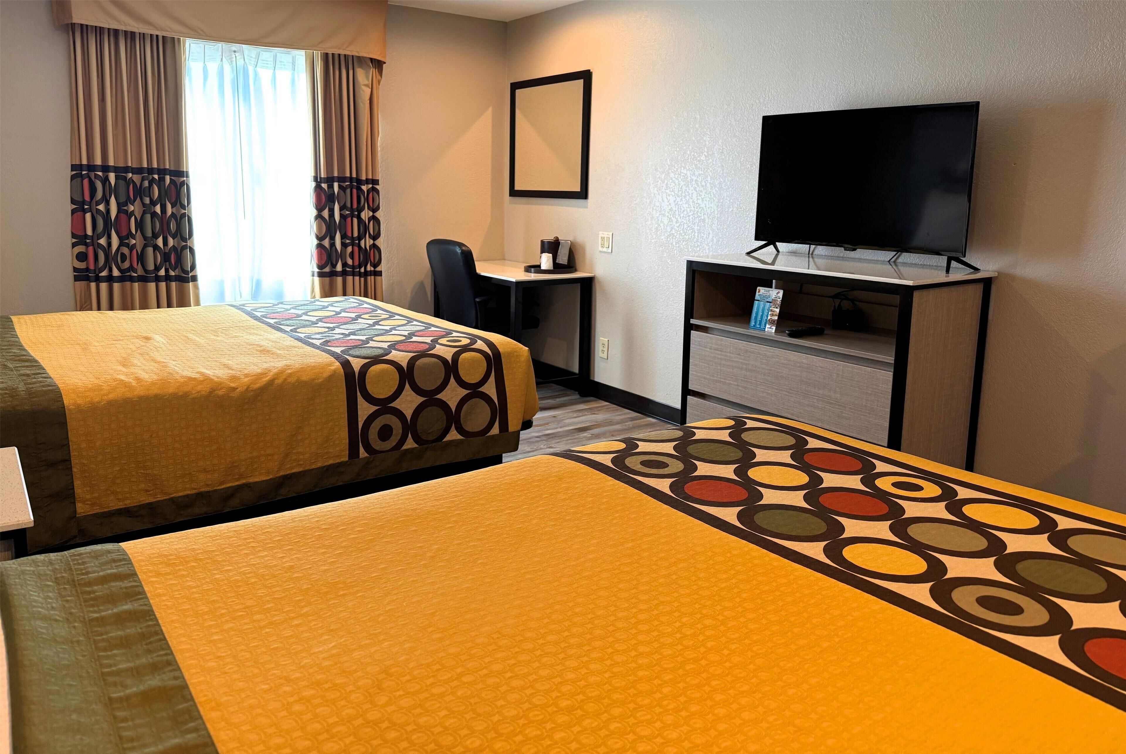 A hotel room with two beds, a desk, a television, and a window with curtains.