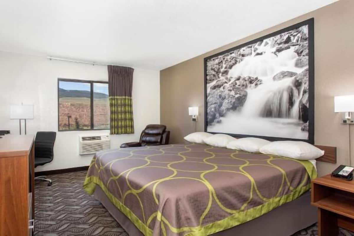 Ein Hotelzimmer mit Bett, Schreibtisch mit Fernseher, Sessel, Fenster mit Blick und einem großen Gemälde eines Wasserfalls.
