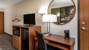 A hotel room with a wooden desk, a television, a coffee maker, a microwave, and a mirror.