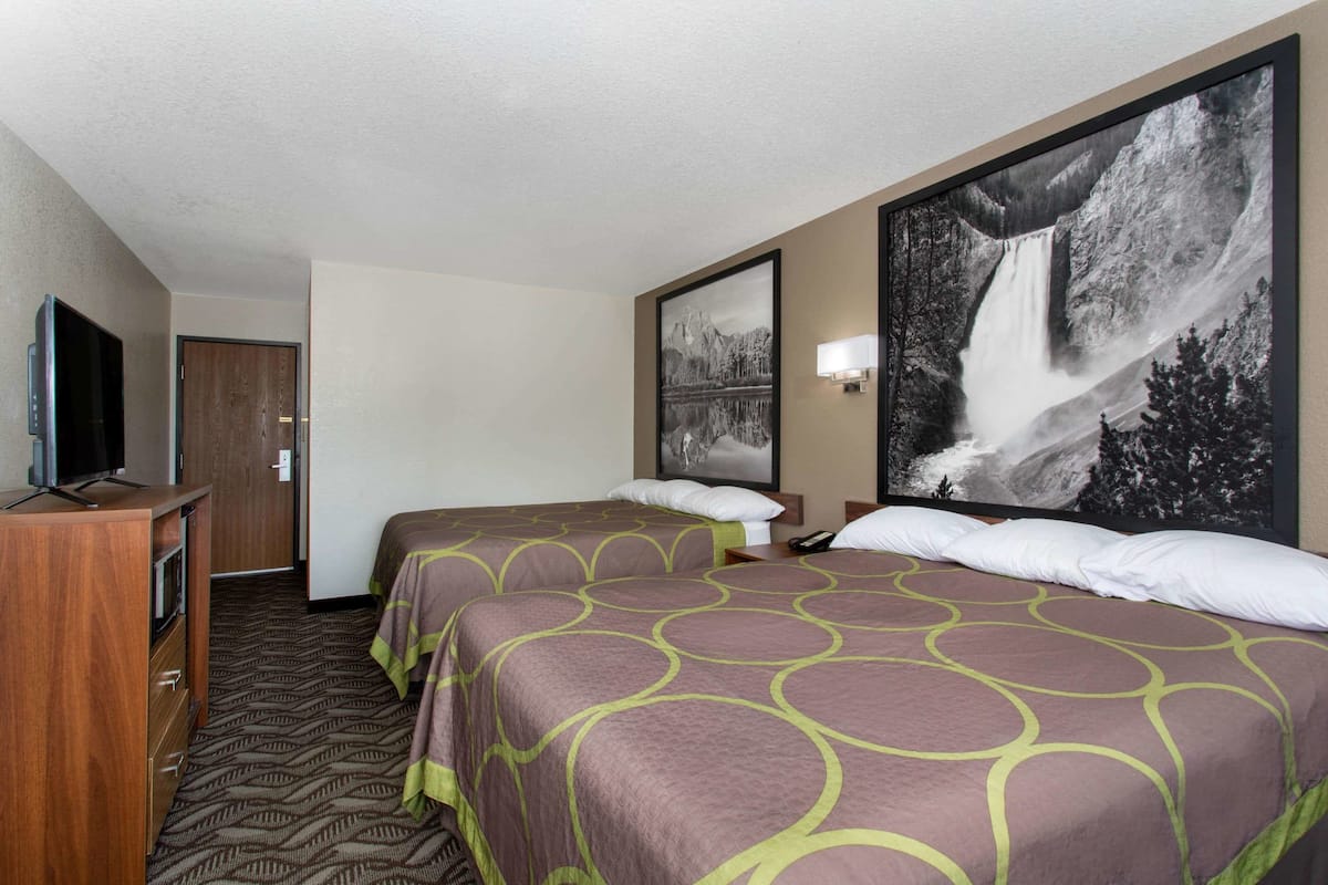Ein Hotelzimmer mit zwei Betten, einem Fernseher, einem Schreibtisch und einem großen Wandbild mit einem Wasserfall.