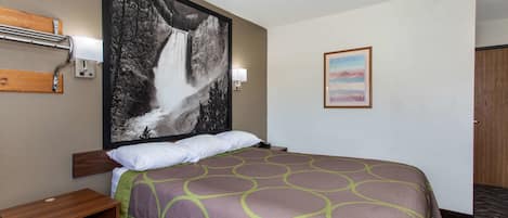 A hotel room with a large bed, a wooden headboard, a nightstand, a wall-mounted lamp, a framed picture of a waterfall, and a carpeted floor.