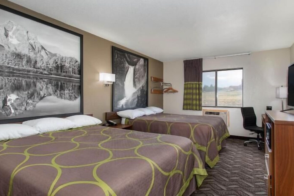 A hotel room with two beds, a desk, a TV, and large landscape paintings on the walls.