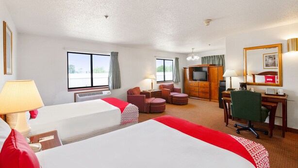 Een hotelkamer met twee bedden, een bureau, een stoel, een televisie en een groot raam.
