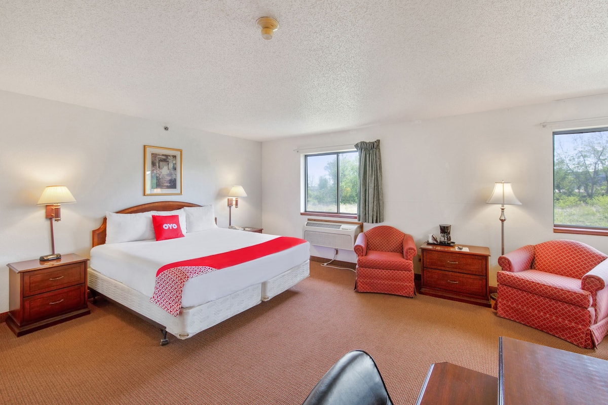 A hotel room with a large bed, two bedside tables, a desk, a chair, and a window with curtains.