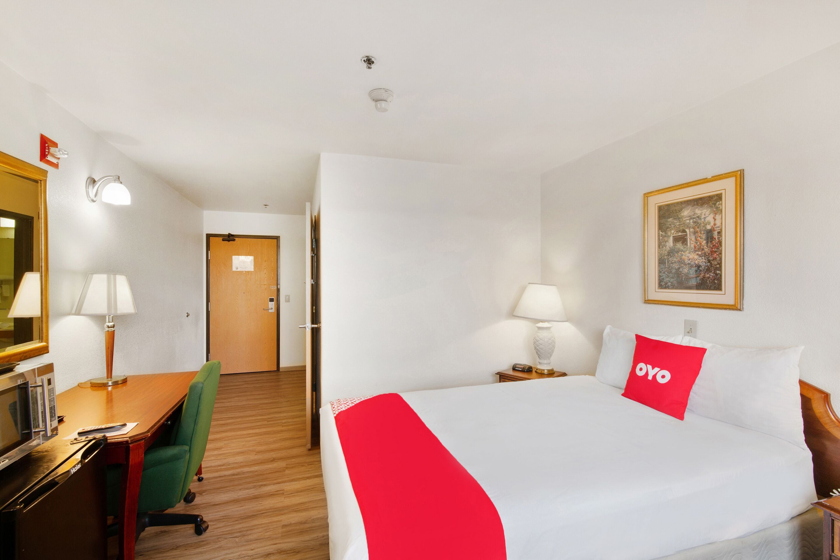 A hotel room with a bed, desk, chair, and a door leading to another room.