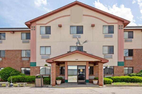 Un hotel a più piani con facciata beige, un ingresso centrale con tetto marrone e un'antenna parabolica sul tetto.