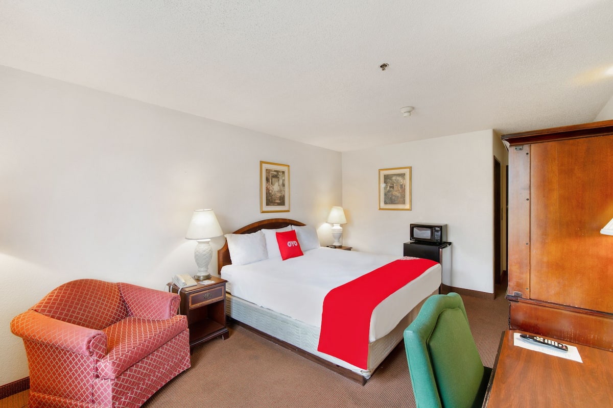 A hotel room with a bed, two bedside lamps, a chair, a desk, and a television.